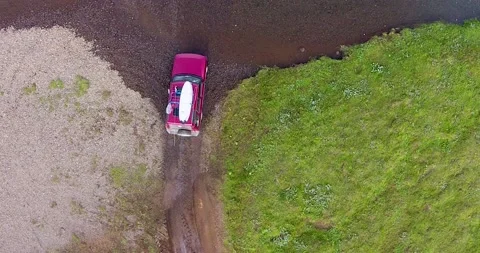 A top down view of a red SUV crossing through a river with a surfboard Stock Footage 234820423
