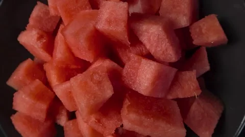 Top down view of red watermelon cubes that are sliced in a bowl on a dark black Stock Footage 314501214