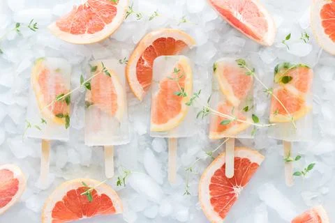 Top down view of a row of grapefruit and thyme popsicles laying on a bed of ice. Stock Photos