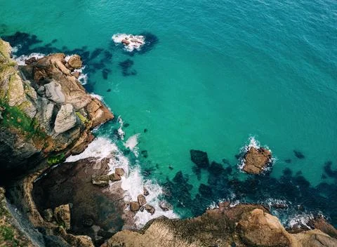 Top down view of rugged coastal cliffs and turquoise waters crashing against Stock Photos