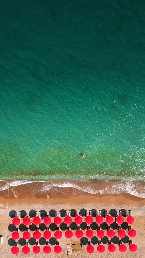 Top-down view of sandy beach with red sun umbrellas and turquoise sea water Stock Footage 301542829