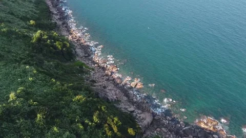 Top down view shoreline from cliff with lush greenery, rocks and blue calm ocean Stock Footage 131821472