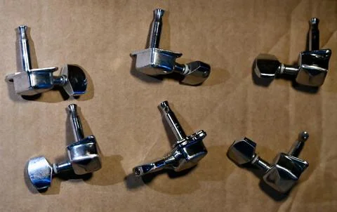 Top-down view of six chrome electric guitar tuning pegs on a brown background Stock Photos