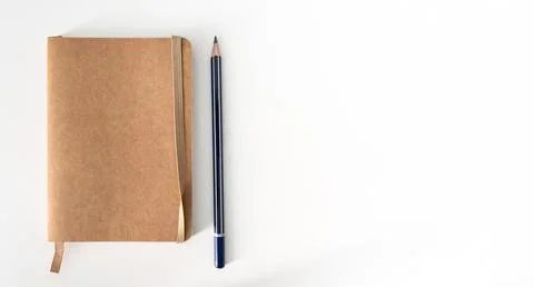Top down view of small brown notebook and sharp pencil on white desk Stock Photos