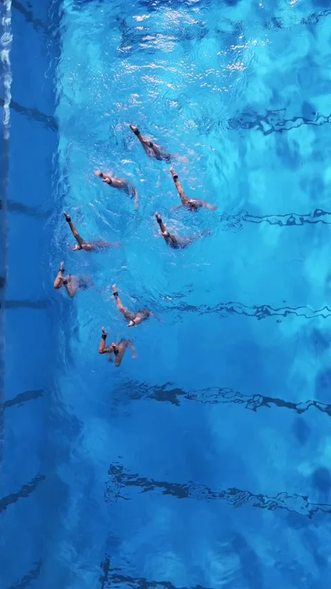 Top-down view of synchronized swimmers performing in a clear blue pool. Video stock 297472889
