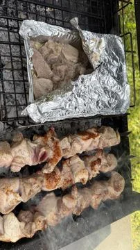 Top-down view of three meat skewers and an open foil tray of tender meat Stock Photos