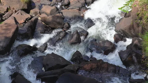 Top-down view of turbulent water flowing through large dark boulders 库存影片 335230778