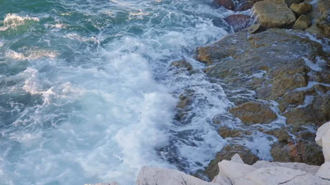 Top down view of turquoise sea waves crashing against a rocky shore. White fo Vídeo Stock 326671155