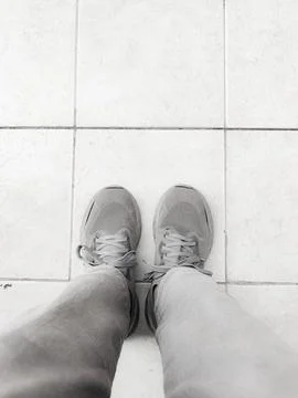 Top-down view of two feet wearing gray sneakers and light gray pants, standing o Stock Photos