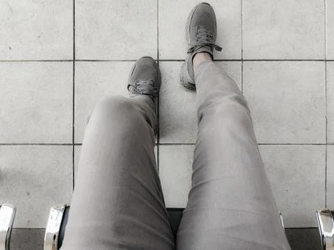 Top-down view of two feet wearing gray sneakers and light gray pants, standing o Stock Photos
