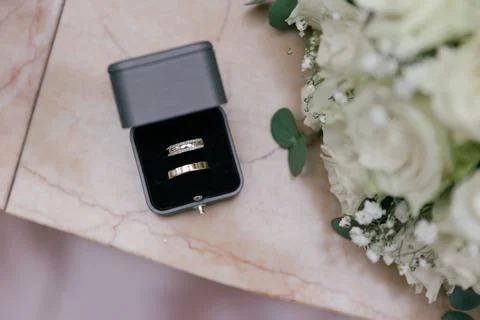 Top-down view of two gold wedding bands sitting inside an open gray ring box on Stock Photos