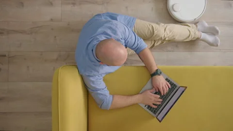 Top down view of unrecognizable bald man in blue shirt, sitting on floor next to Stock Footage 243362320