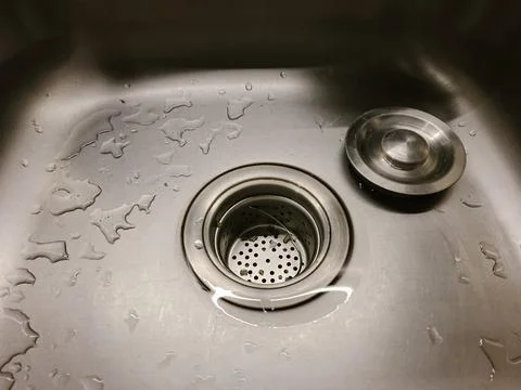Top-down view of a wet stainless steel kitchen sink with a strainer basket .. Stock Photos