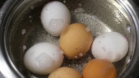 Top-down view of white and brown chicken eggs cooking in a pot of hot boiling Stock Footage 319633116