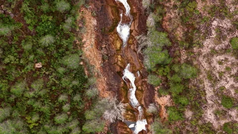 Top-down view of a white rushing stream cutting through red rocky terrain Видео 334785737