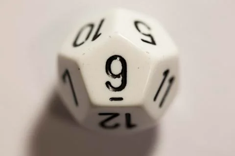 Top-down view of a white twelve sided die, showing a nine Photos