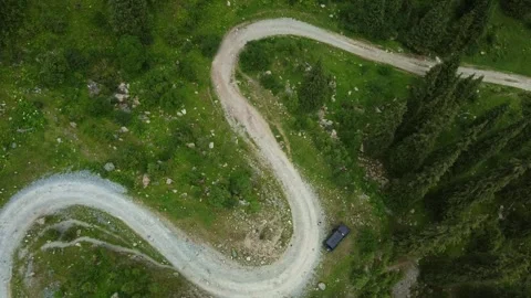 Top down view of winding mountain dirt road with off-road car in green forest Видео 334326237