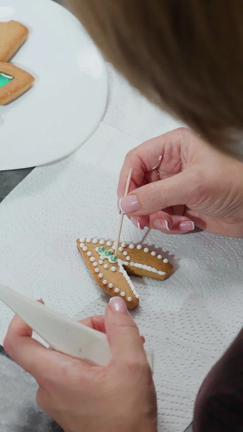 Top-down view of woman decorating cookies with icing and adjusting green bead Stock Footage 320345701