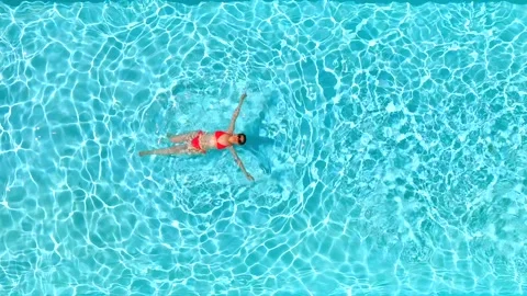 Top down view of a woman in pink swimsuit swimming on her back in the pool. Video stock 326533880