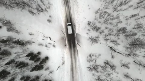 Top drone view of a van driving along a snowy asphalt road amid a frozen Nordic Stock Footage 330376583