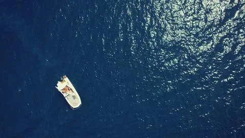 Top drone view of a white small boat floating on the surface of dark-blue calm Stock Photos