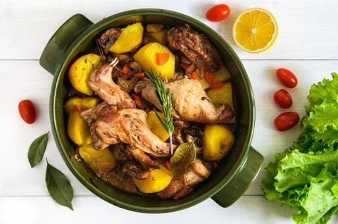 Top flat view of roasted rabbit meat with vegetables in round ceramic pot on Stock Photos