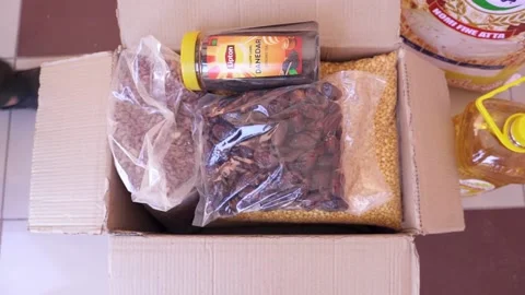 Top shot of a box that is filled with basic food items. A man puts the last item 動画素材 165841672