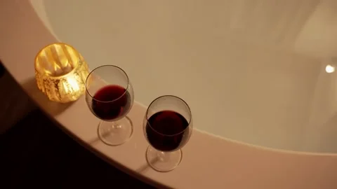 Top shot overhead showing two glasses of wine next to bathtub and a candle Stock Footage 154212446