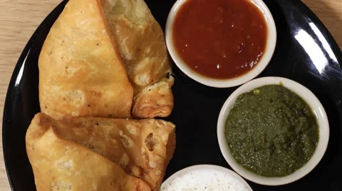 Top-shot track-in close-up of a plate of Samosa served with condiments Stock Footage 62923545