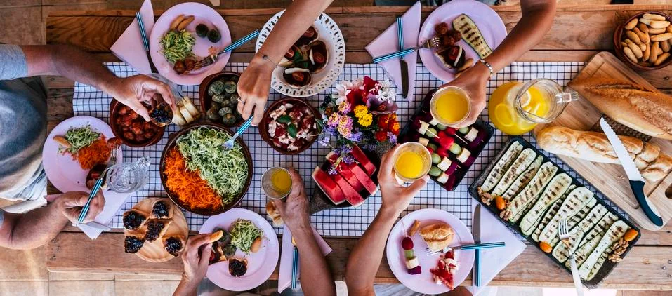 Top vertical view of table full of food and drinks and happy people friends c Stock Photos