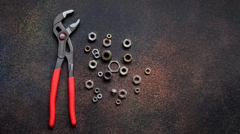 Top view of adjustable universal pliers for repair and assorted nuts on dark Stock Photos