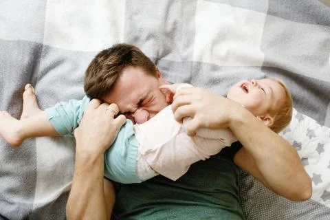 Top view of affectionate young father holding his baby daughter kid and tickl
