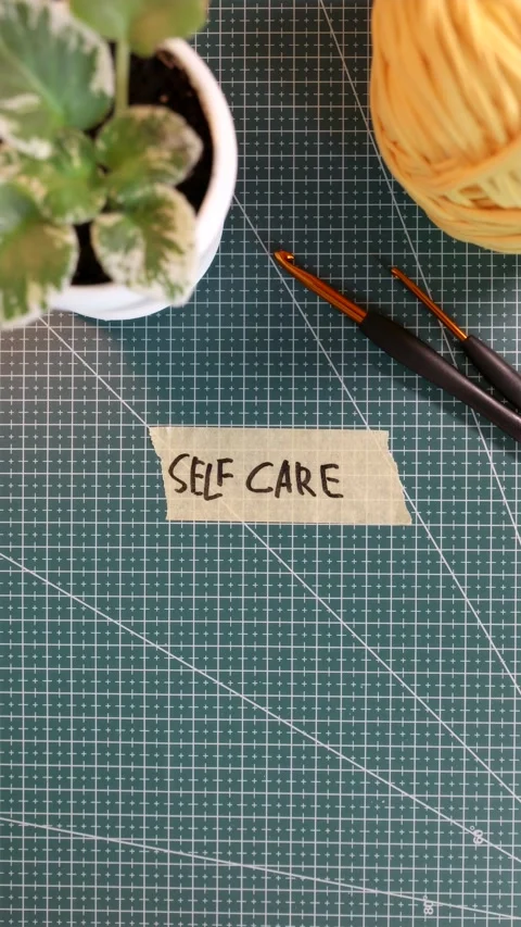 Top view of applying SELF CARE tape sticker near flowerpot and yarn ball Stock Footage 338183532