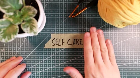 Top view of applying SELF CARE tape sticker near flowerpot and yarn ball. Stock Footage 338183818