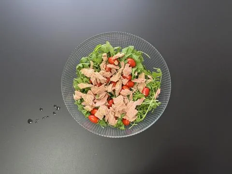 Top view of arugula salad with cherry tomatoes and canned tuna in glass bowl Stockfoto's