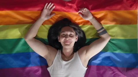 Top view of asian young man lying on rainbow flag and looking at camera Video stock 243641392