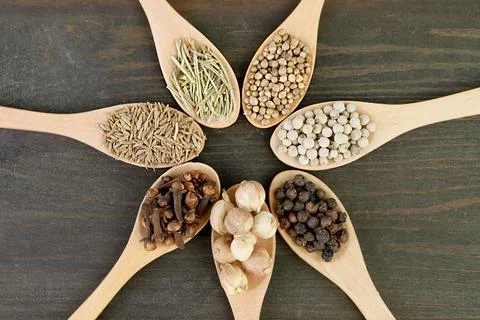 Top view of assorted aromatic spices in wooden spoons on black wooden backdrop Stock Photos