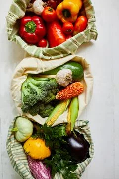 Top view assorted fresh vegetables in reusable cotton bags on table in the ki Stock Photos