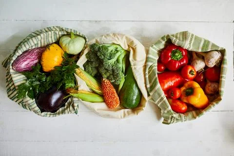 Top view assorted fresh vegetables in reusable cotton bags on table in the ki Stock Photos