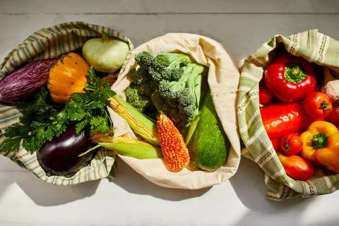 Top view assorted fresh vegetables in reusable cotton bags on table in the ki Stock Photos