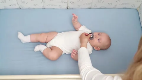 Top view of baby lying in crib, mom giving him pacifier, stroking infant's head Stock Footage 297836002