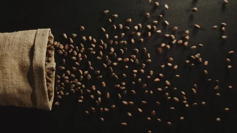 TOP VIEW: Bag falls and unpeeled pine nuts are poured out of it - Slow Motion Stock Footage 98385086