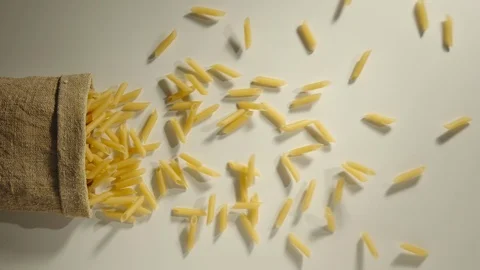 TOP VIEW: Bag falls and penne rigate are poured out of it on white - Slow Motion Stock Footage 98666280