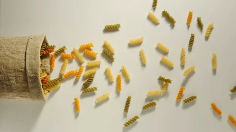 TOP VIEW: Bag falls and colored curly pasta are poured out of it  - Slow Motion Stock Footage 98666310