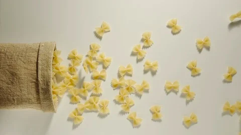 TOP VIEW: Bag falls and pasta letters are poured out of it on white- Slow Motion Video stock 98666319