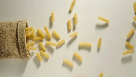 TOP VIEW: Bag falls and tortiglioni are poured out of it on white - Slow Motion Stock Footage 98666326