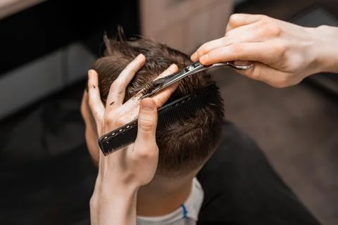 Top view barber uses scissors and comb to style the mans hair at the barbershop. Stock Photos
