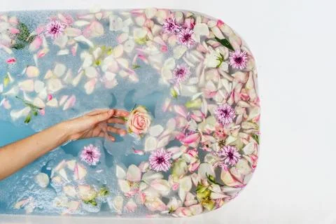 Top view of bath filled with blue bubble water, flowers and petals with woman Foto stock