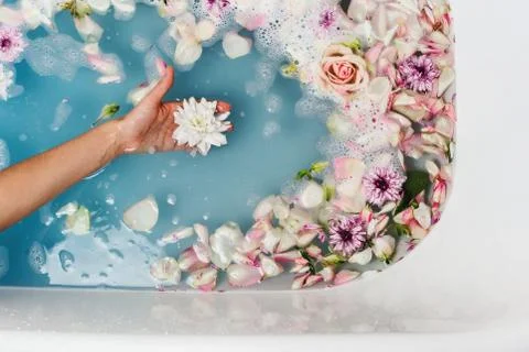 Top view of bath filled with blue bubble water and petals with woman's hand h Stock Photos