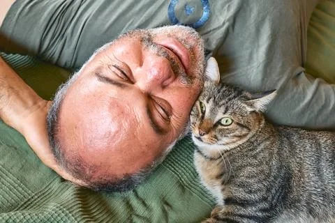 Top view of bearded middle-aged man lying on a bed and playing with his gra.. Stock Photos